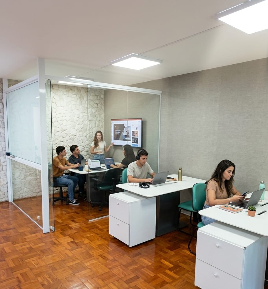 Estações de trabalho compartilhadas da playINwork ao lado de uma sala de reunião com divisória de vidro