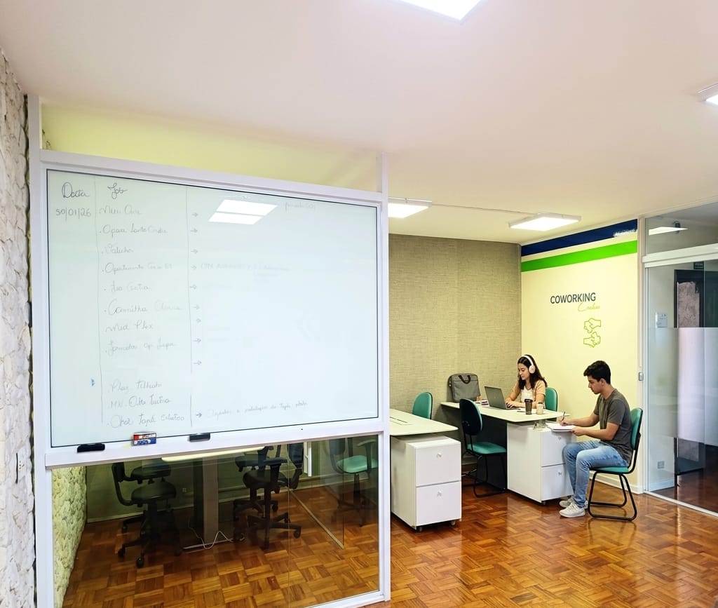 Área de recepção da playINwork com lousa branca, estações de trabalho e sala envidraçada